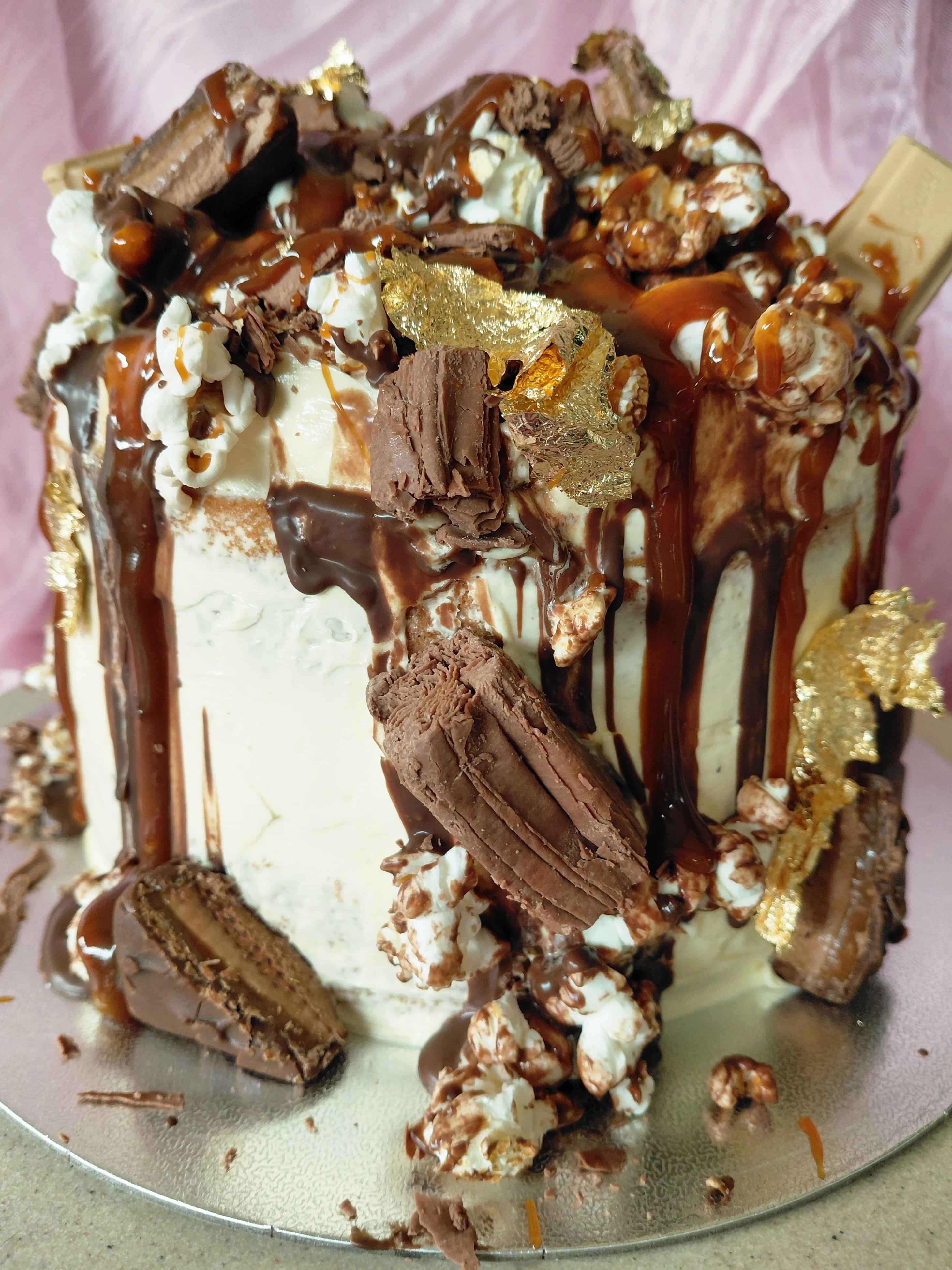 Indulgent vanilla cake with vanilla buttercream, caramel and chocolate sauce, caramel pop corn and chocolates on top