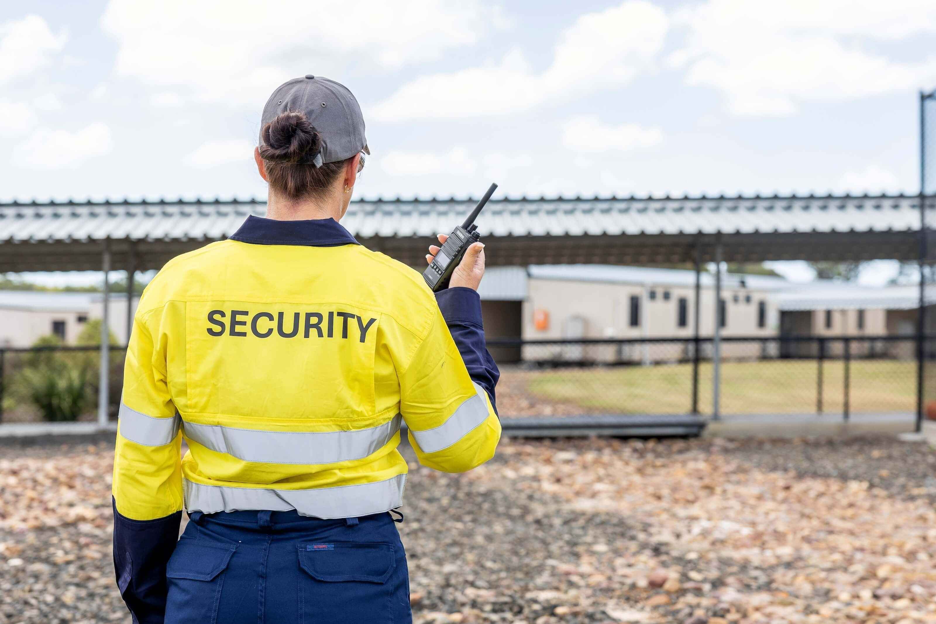 The back of a woman wearing a security shirt and holding a walkie talkie.