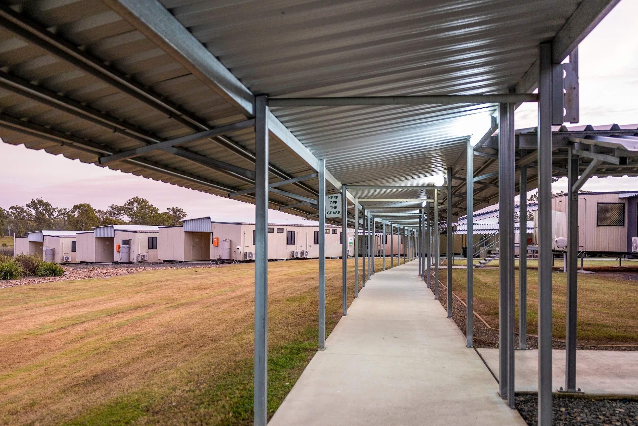 A covered cement path leads to accommodation rooms and is near lawn.